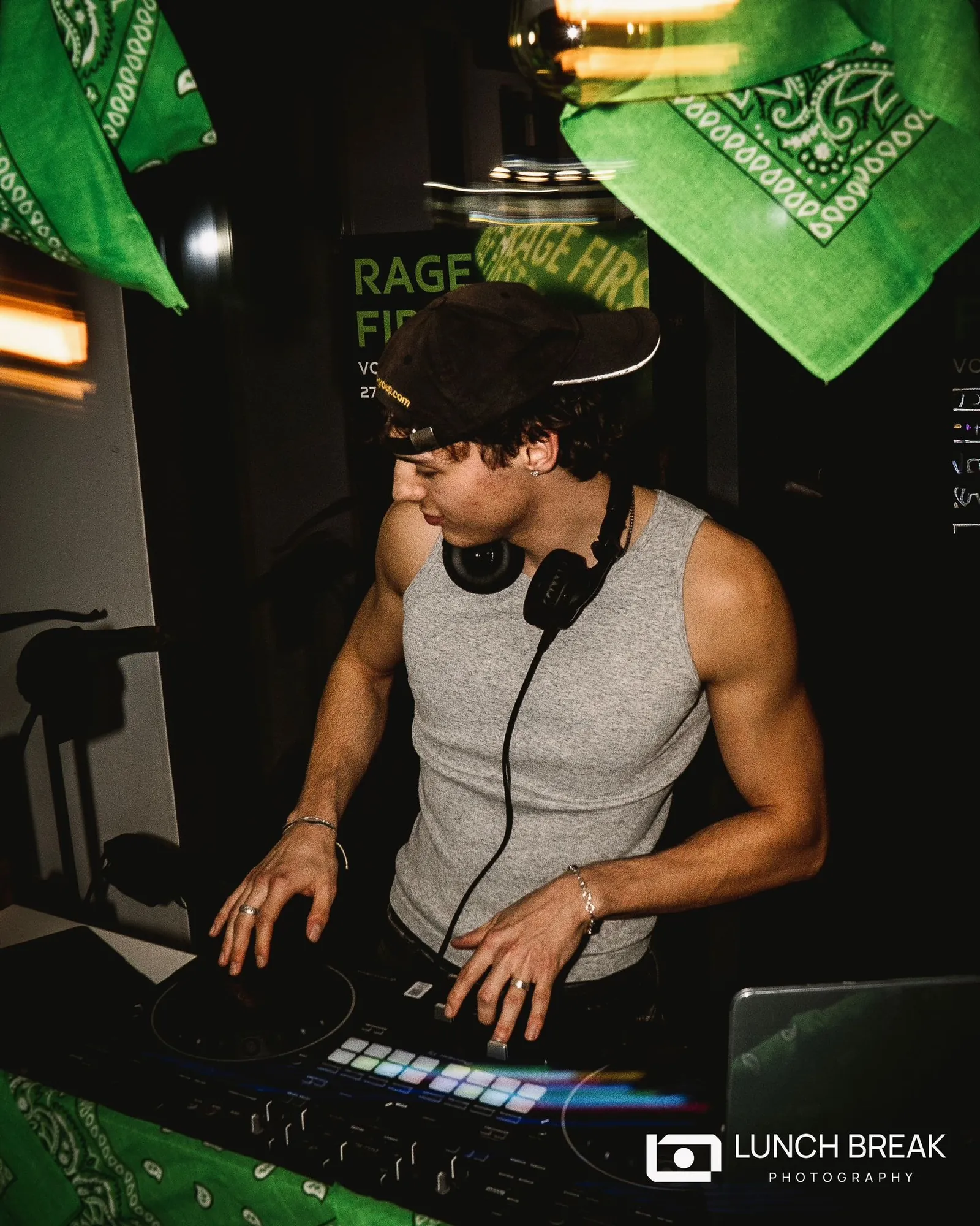 Samu alias DJ Muél am DJ-Pult, weißes Tanktop, Kopfhörer um den Hals, grüne Bandanas über der Booth